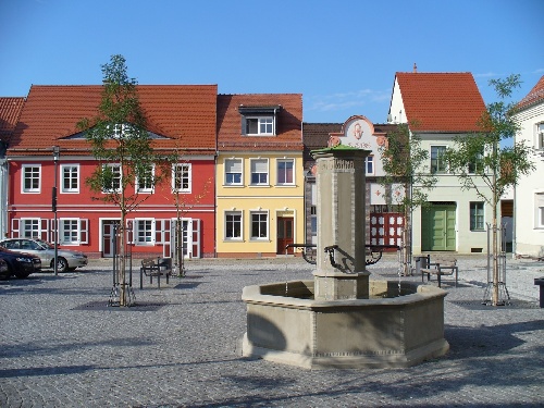 Historischer Marktplatz in Spremberg mit Brunnen, sanierten Bürgerhäusern und gepflastertem Platz bei sonnigem Wetter.